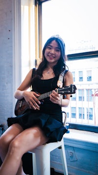 a young woman playing an ukulele in front of a window